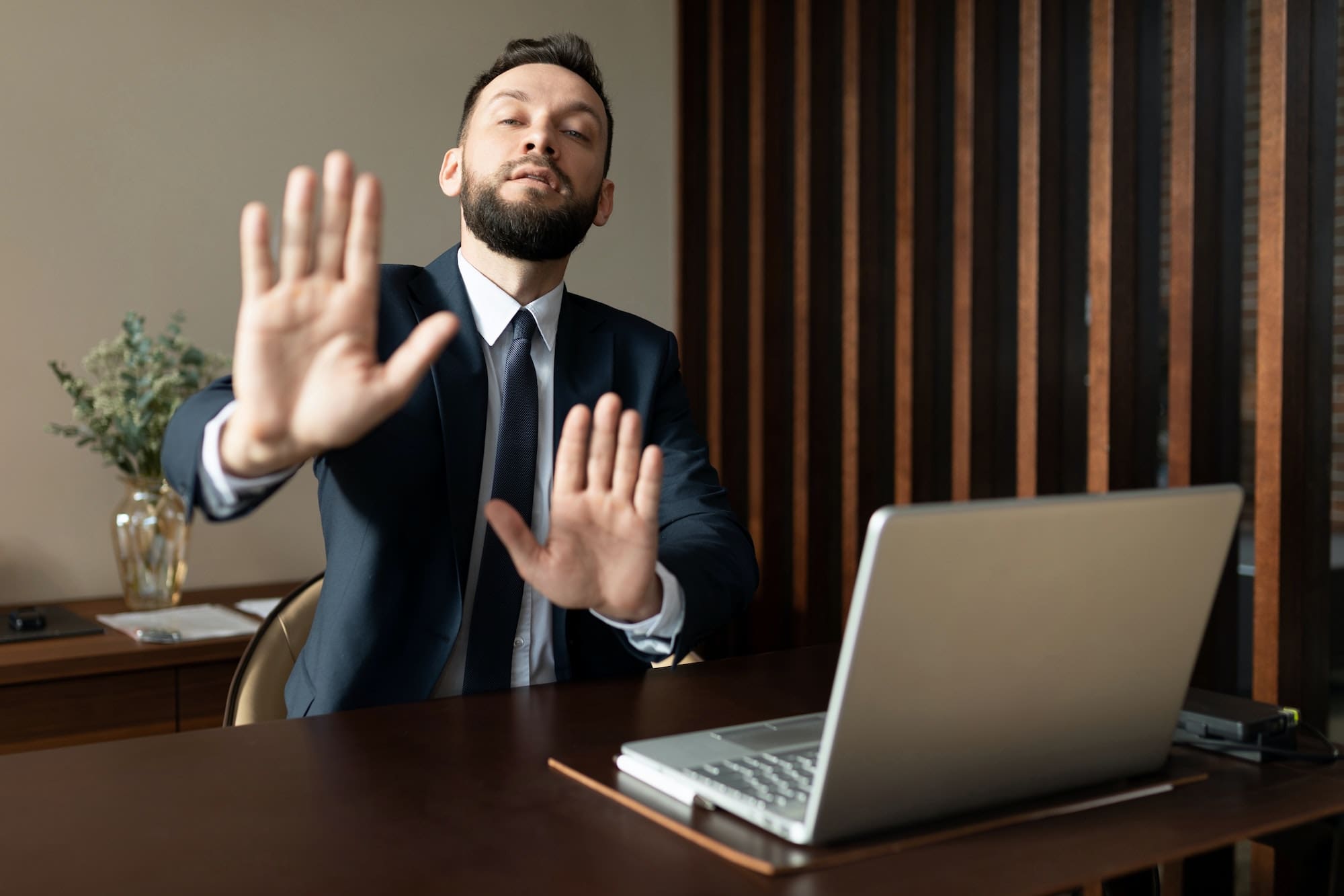 businessman with the palms of his hands demonstrates refusal while sitting at a laptop in the office