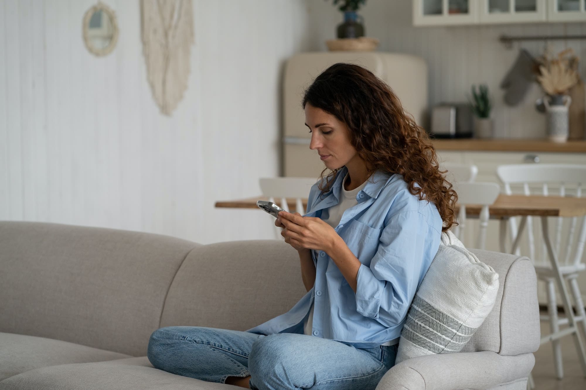 Concentrated introverted woman with smartphone sit on sofa with legs tucked under in living room